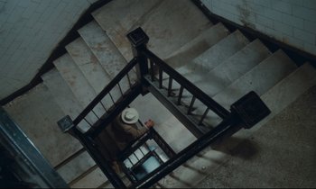 Movie still from “Atlantic City” (1980), directed by Louis Malle – A man with a hat walking up a flight of stairs; Extreme Wide shot, Overhead angle