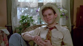 Movie still from “Sophie's Choice” (1982), directed by Alan J. Pakula – A man wearing a hat and a tie sitting in a chair; Medium shot, Low angle