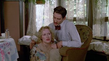 Movie still from “Sophie's Choice” (1982), directed by Alan J. Pakula – A woman sitting on a man's lap in a living room; Medium shot, Low angle