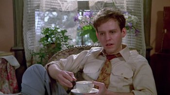 Movie still from “Sophie's Choice” (1982), directed by Alan J. Pakula – A man sitting in a chair holding a cup of coffee; Medium shot, Low angle