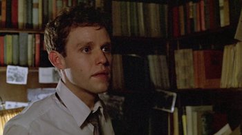 Movie still from “Sophie's Choice” (1982), directed by Alan J. Pakula – A young man in a white dress shirt and tie in front of bookshelves; Close Up shot, Low angle