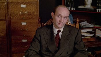 Movie still from “Sophie's Choice” (1982), directed by Alan J. Pakula – A man in a suit and tie sitting in a chair in front of a filing cabinet; Close Up shot, High angle