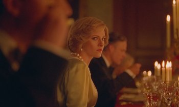 Movie still from “Spencer” (2021), directed by Pablo Larraín – A woman in a white dress is sitting in front of a group of people; Close Up shot, Over the shoulder angle
