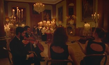 Movie still from “Spencer” (2021), directed by Pablo Larraín – A group of people sitting around a room with candles; Extreme Wide shot, High angle