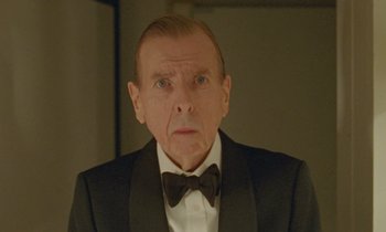 Movie still from “Spencer” (2021), directed by Pablo Larraín – An older man wearing a suit and a bow tie; Close Up shot, Low angle