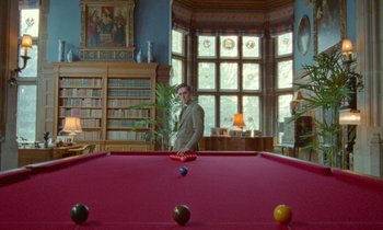 Movie still from “Spencer” (2021), directed by Pablo Larraín – A man standing in front of a red pool table; Wide shot, Low angle