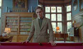 Movie still from “Spencer” (2021), directed by Pablo Larraín – A man in a suit stands at the edge of a pool table; Medium shot, Low angle