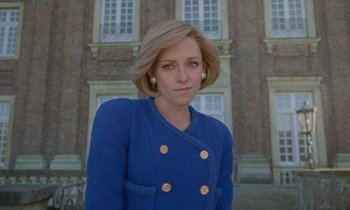 Movie still from “Spencer” (2021), directed by Pablo Larraín – A woman in a blue jacket standing in front of a building; Medium shot, Low angle
