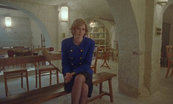 Movie still from “Spencer” (2021), directed by Pablo Larraín – A woman sitting on top of a wooden bench in a room; Wide shot, High angle