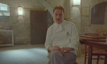 Movie still from “Spencer” (2021), directed by Pablo Larraín – A man sitting in a room wearing a chef's outfit; Medium shot, Low angle