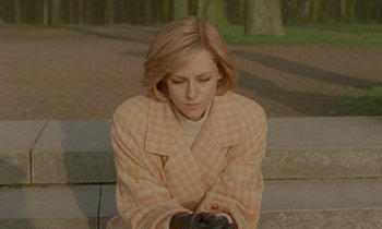 Movie still from “Spencer” (2021), directed by Pablo Larraín – A woman sitting on steps looking down at her cell phone; Medium shot, High angle