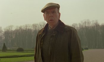 Movie still from “Spencer” (2021), directed by Pablo Larraín – An older man wearing a hat and a jacket; Medium shot, Low angle