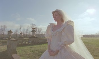 Movie still from “Spencer” (2021), directed by Pablo Larraín – A woman in a wedding dress standing in a field; Medium shot, Low angle