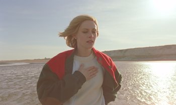 Movie still from “Spencer” (2021), directed by Pablo Larraín – A woman standing on the beach with her hands on her chest; Close Up shot, Over the shoulder angle