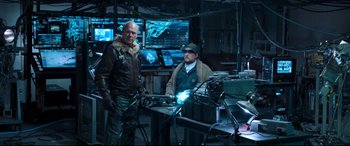 Movie still from “Spider-Man: Homecoming” (2017), directed by Jon Watts – Two men standing next to each other in front of a machine; Medium shot, Over the shoulder angle