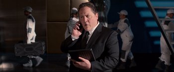 Movie still from “Spider-Man: Homecoming” (2017), directed by Jon Watts – A man in a suit and tie on a cell phone and holding a laptop; Medium shot, Over the shoulder angle