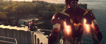 Movie still from “Spider-Man: Homecoming” (2017), directed by Jon Watts – A man sitting on top of a building next to a building; Wide shot, Over the shoulder angle