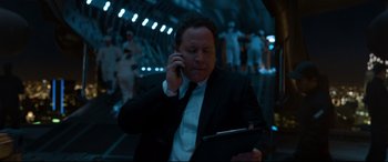 Movie still from “Spider-Man: Homecoming” (2017), directed by Jon Watts – A man in a suit and tie on a cell phone and holding a tablet computer; Medium shot, Low angle