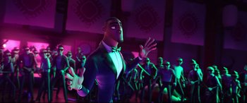 Movie still from “Spies in Disguise” (2019), directed by Troy Quane – A man in a suit and bow tie standing in front of a group of people; Medium shot, Low angle
