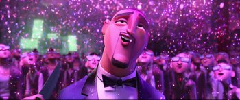 Movie still from “Spies in Disguise” (2019), directed by Troy Quane – A man in a suit and bow tie is smiling in front of a bunch of people; Close Up shot, Low angle