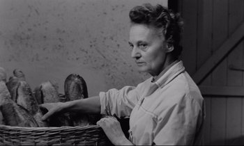 An older woman is holding a basket of bread