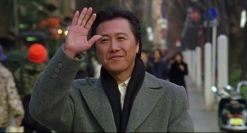 A man in a gray coat waving at the camera