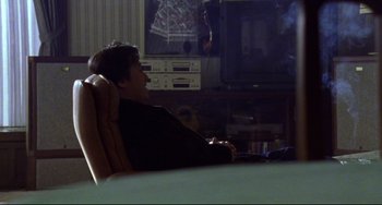 Movie still from “Audition” (1999), directed by Takashi Miike – A man sitting in front of a tv in a room; Medium shot, Over the shoulder angle