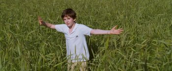 Movie still from “August Rush” (2007), directed by Kirsten Sheridan – A young boy standing in tall grass with his arms outstretched; Medium shot, Low angle