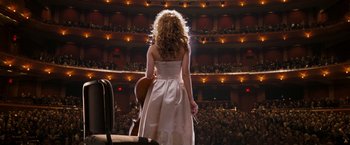 Movie still from “August Rush” (2007), directed by Kirsten Sheridan – A woman standing in front of an audience holding a cello; Wide shot, High angle