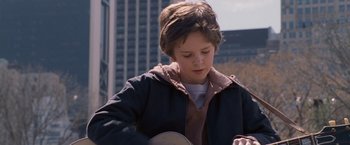 Movie still from “August Rush” (2007), directed by Kirsten Sheridan – A young boy is playing a guitar outside; Close Up shot, Over the shoulder angle