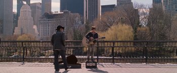 Movie still from “August Rush” (2007), directed by Kirsten Sheridan – A man playing a guitar while another man stands on a bench; Wide shot, Over the shoulder angle