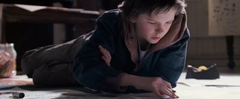 Movie still from “August Rush” (2007), directed by Kirsten Sheridan – A young boy laying on the ground looking at a paper; Close Up shot, Overhead angle