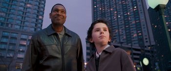 Movie still from “August Rush” (2007), directed by Kirsten Sheridan – A man and a boy standing next to each other in front of a building; Medium shot, Low angle