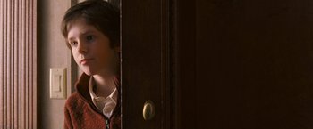 Movie still from “August Rush” (2007), directed by Kirsten Sheridan – A young man standing in a room next to a wooden door; Close Up shot, Over the shoulder angle