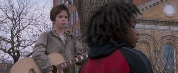 Movie still from “August Rush” (2007), directed by Kirsten Sheridan – A young man playing a guitar in front of a tree; Medium shot, Over the shoulder angle