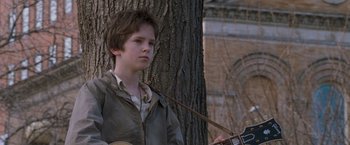 Movie still from “August Rush” (2007), directed by Kirsten Sheridan – A young boy holding a guitar in front of a tree; Close Up shot, Low angle