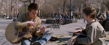 Movie still from “August Rush” (2007), directed by Kirsten Sheridan – A man playing a guitar on the sidewalk; Medium shot, Low angle
