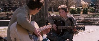Movie still from “August Rush” (2007), directed by Kirsten Sheridan – Two young men sitting on the ground with guitars; Medium shot, Over the shoulder angle