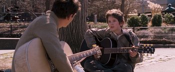 Two young men are playing guitar in a park