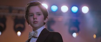 Movie still from “August Rush” (2007), directed by Kirsten Sheridan – A young boy in a suit and bow tie in front of lights; Close Up shot, Low angle