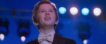 Movie still from “August Rush” (2007), directed by Kirsten Sheridan – A boy in a suit and a bow tie smiling; Close Up shot, Low angle