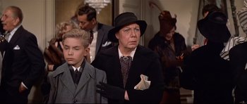 Movie still from “Auntie Mame” (1958), directed by Morton DaCosta – An older woman wearing a black hat and holding a napkin; Medium shot, Over the shoulder angle