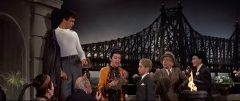 Movie still from “Auntie Mame” (1958), directed by Morton DaCosta – A group of people standing next to each other on a bridge; Medium shot, Low angle