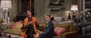 Movie still from “Auntie Mame” (1958), directed by Morton DaCosta – A woman and a young boy sitting on a couch; Medium shot, Low angle