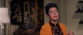 Movie still from “Auntie Mame” (1958), directed by Morton DaCosta – An older woman wearing a yellow jacket and a black hat; Close Up shot, Over the shoulder angle