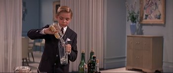 Movie still from “Auntie Mame” (1958), directed by Morton DaCosta – A young boy in a suit and tie holding a glass; Medium shot, Low angle