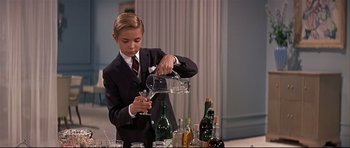 Movie still from “Auntie Mame” (1958), directed by Morton DaCosta – A young boy in a suit pouring a glass of wine into a wine glass; Medium shot, Low angle