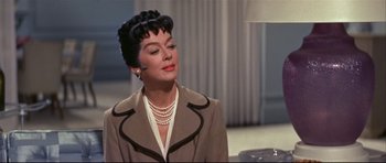Movie still from “Auntie Mame” (1958), directed by Morton DaCosta – A woman in a brown jacket and pearls is looking to the side; Close Up shot, Over the shoulder angle