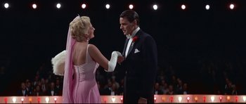 Movie still from “Auntie Mame” (1958), directed by Morton DaCosta – A man and a woman in formal wear holding hands in front of an audience; Medium shot, Low angle