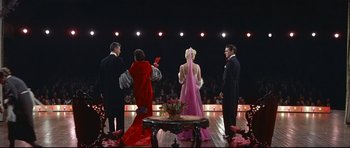 Movie still from “Auntie Mame” (1958), directed by Morton DaCosta – A group of people standing on a stage in front of a crowd; Wide shot, High angle